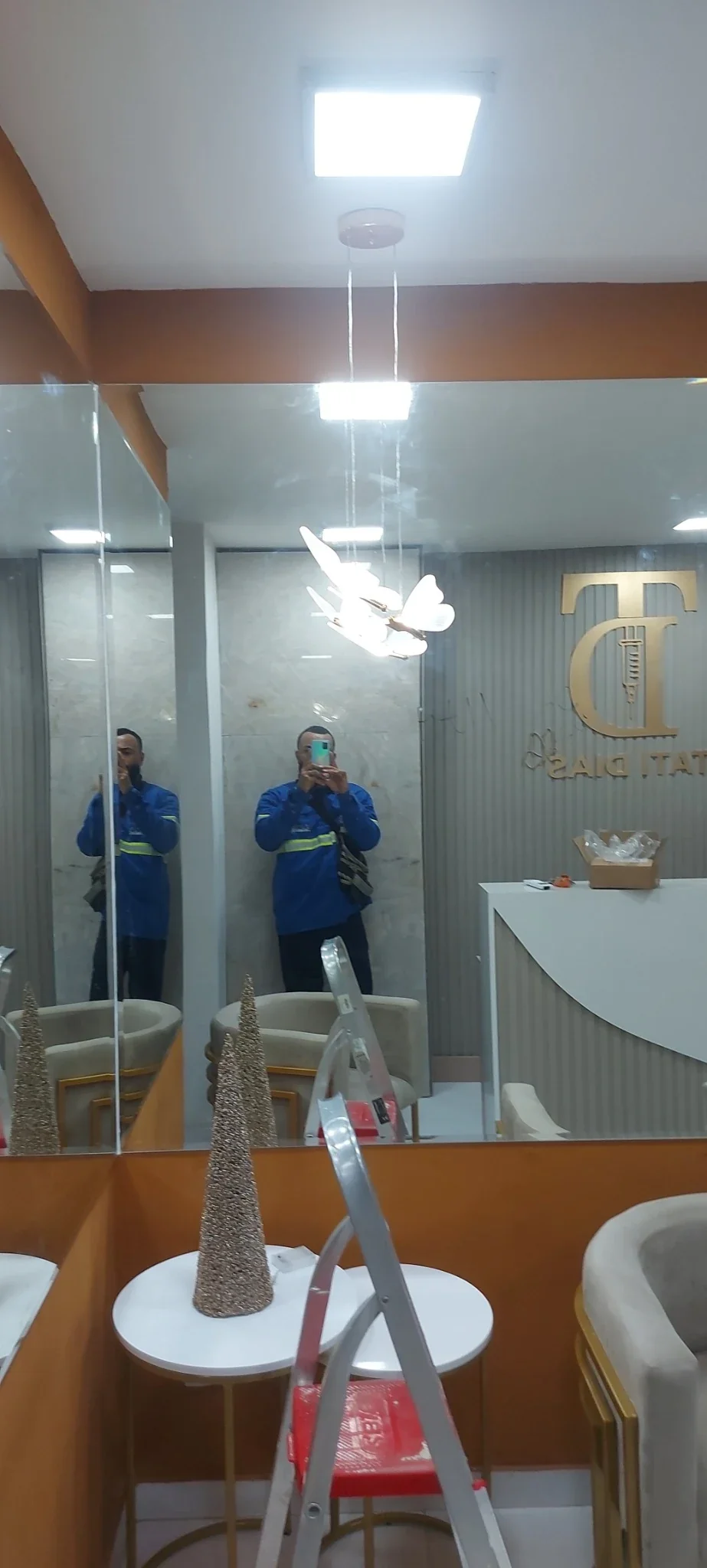 Instalação de iluminação em ambiente comercial com eletricista uniformizado ao fundo.