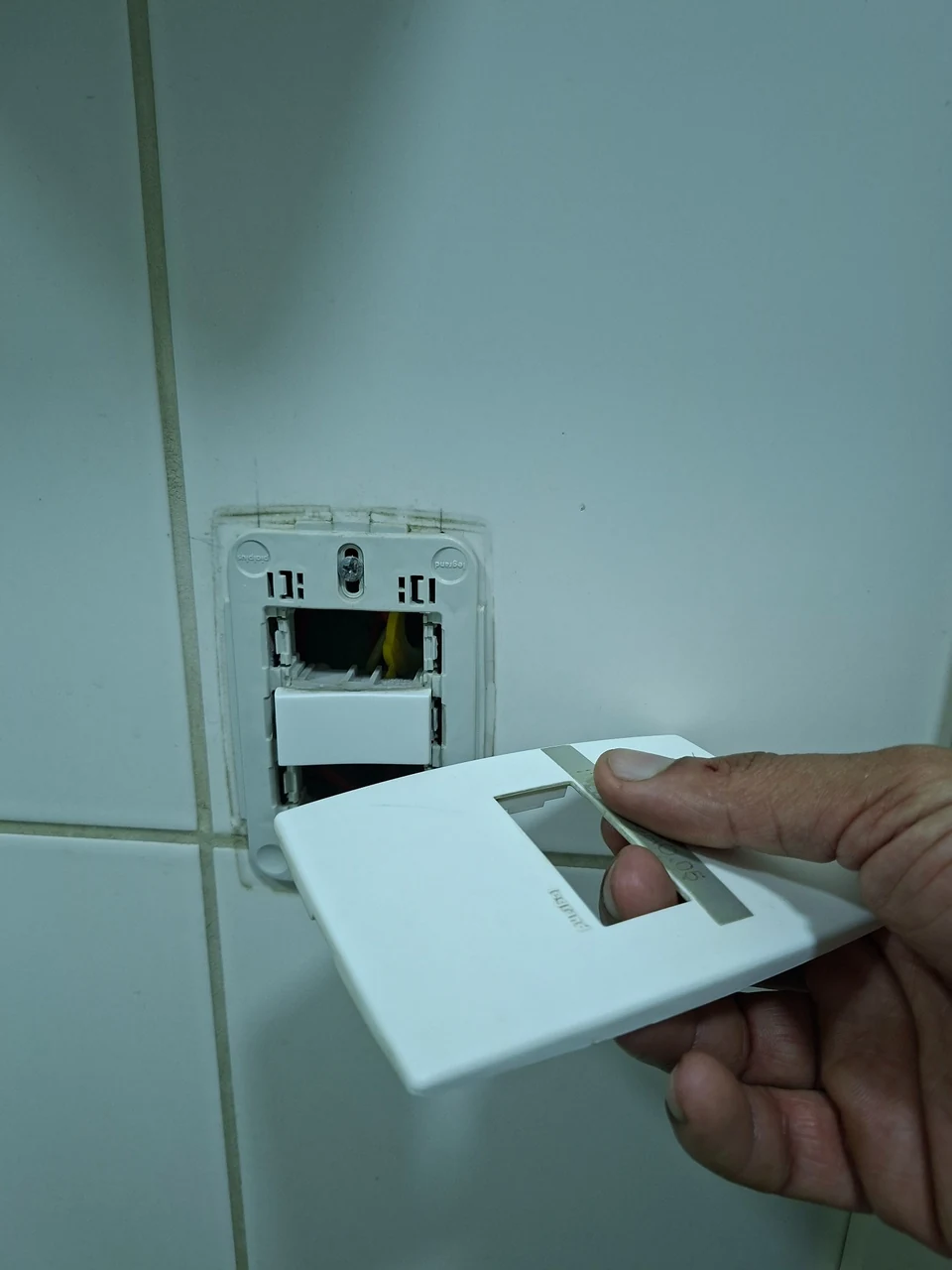 Acabamento de interruptor sendo instalado em parede revestida.